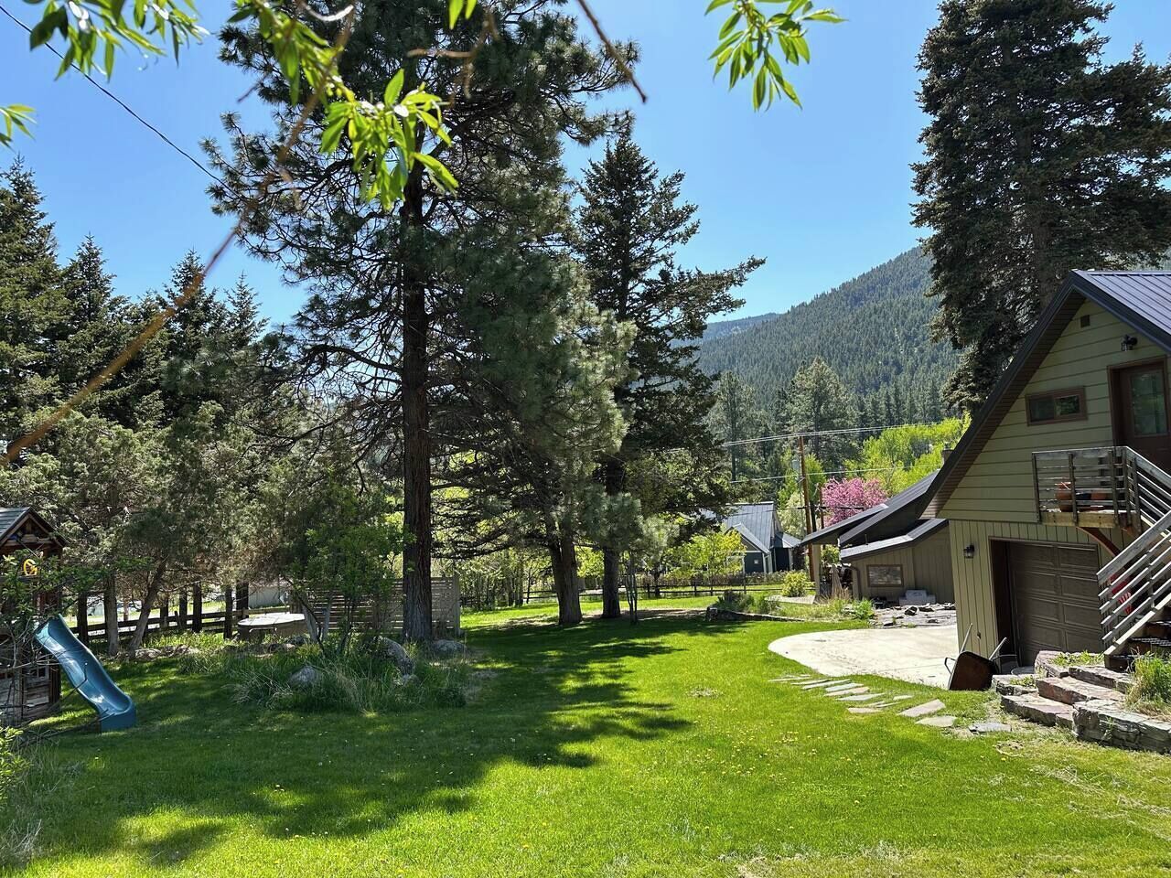 A rural setting with a house, a slide, and a mountain backdrop.