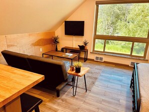 A loft-style living room with a wooden floor, a black sofa, a wooden coffee table, and a TV mounted on the wall. - Helena Forest Nest Studio, Near Downtown (Helena)