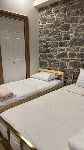 Een kamer met twee eenpersoonsbedden, een stenen muur en een witte deur.
