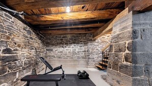 Ein Zimmer mit Steinwänden, einer Sitzbank, Kurzhanteln und einer Treppe.