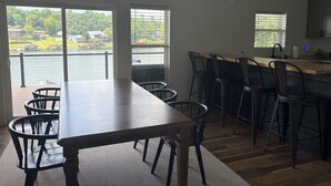 En rummelig spiseplads med søudsigt, et køkken med barstole og store vinduer.