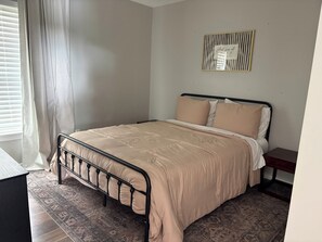 Ein Schlafzimmer mit einem Bett, einem Nachttisch, einem Wandbild und einem gemusterten Teppich.