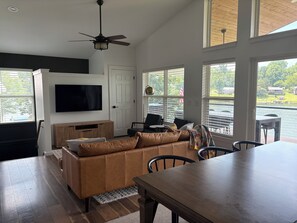 A modern living room with a leather sofa, a flat-screen TV, and a dining table. - Fresh and Modern Lake House Steps to the Water! (Dry Ridge)