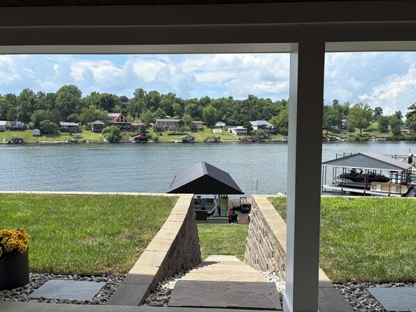 A lakeside view with a covered patio area, a dock with a boat, and a pathway leading to the water. - Fresh and Modern Lake House Steps to the Water! (Dry Ridge)