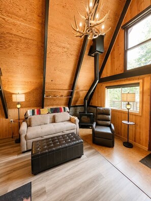 Ein Loft-Zimmer mit einer Couch, einem Hocker und einem Sessel, einem Kamin und einer Chandelüster.