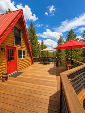 Eine Blockhütte mit roter Tür, einer Terrasse mit Gartenmöbeln und einem roten Sonnenschirm.