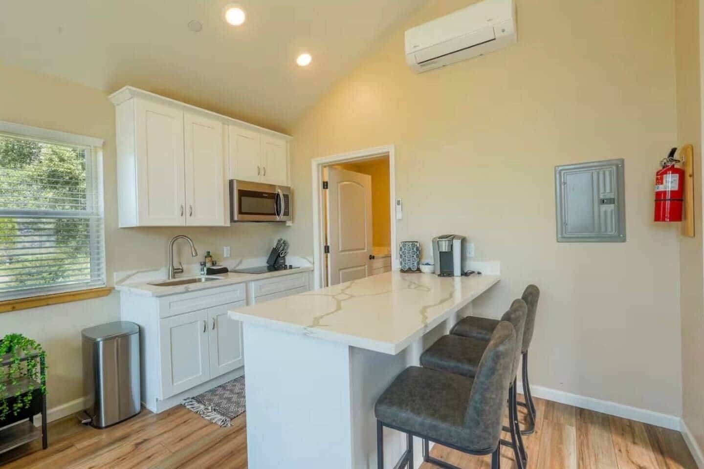 A modern kitchen with white cabinets, a built-in microwave, a coffee machine, and a bar area with stools.
