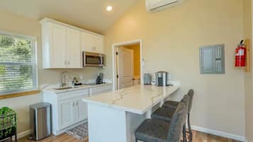 A modern kitchen with white cabinets, a built-in microwave, a coffee machine, and a bar area with stools.