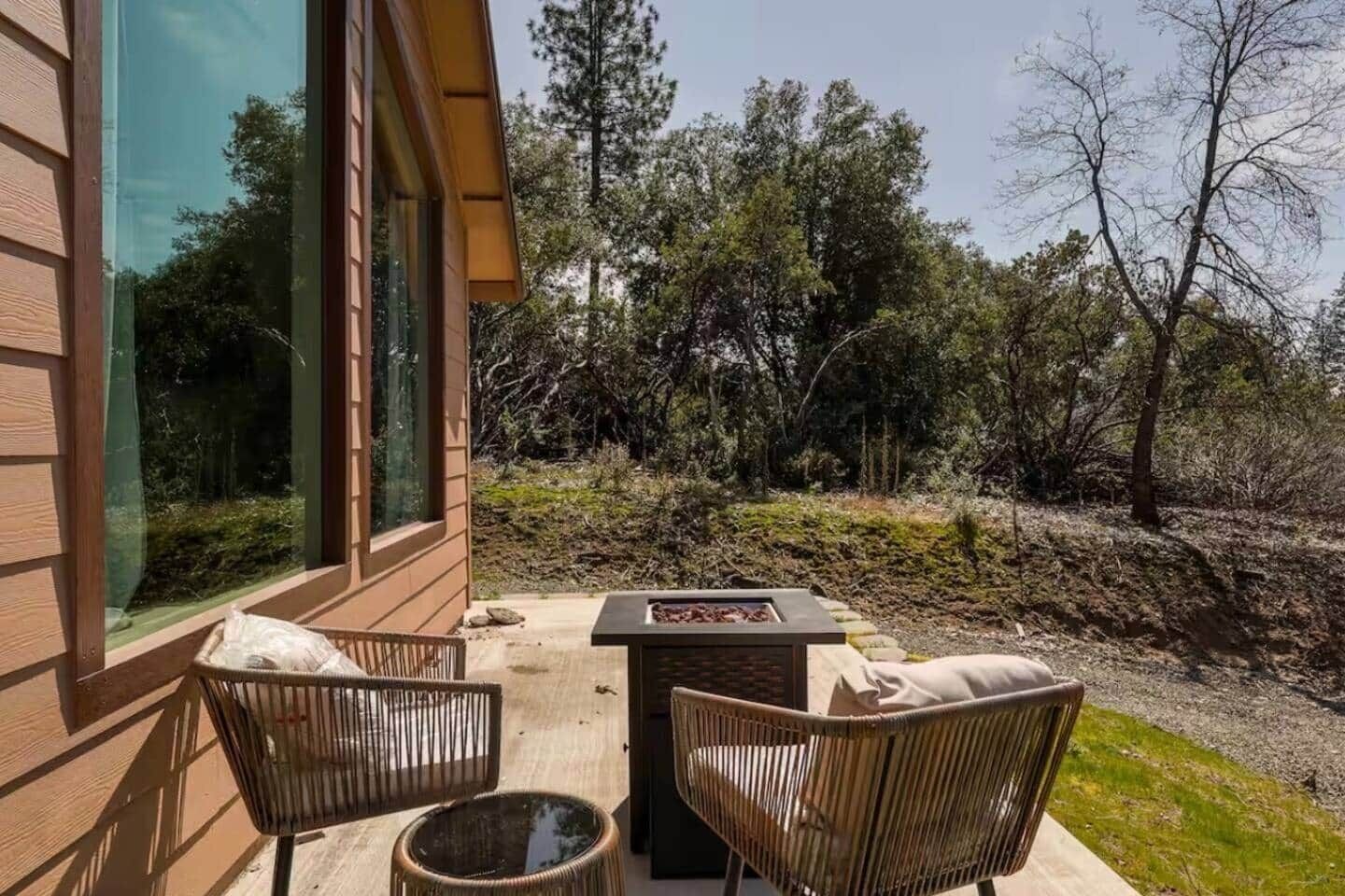 A patio with two wicker chairs and a small table, overlooking a natural landscape with trees and a stone wall.