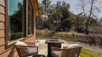 A patio with two wicker chairs and a small table, overlooking a natural landscape with trees and a stone wall.