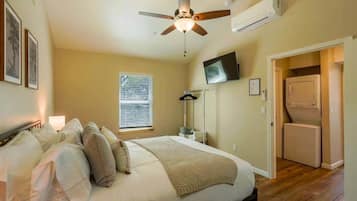 A bedroom with a bed, ceiling fan, TV, and laundry area.