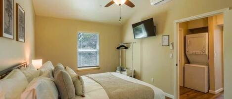 A bedroom with a bed, ceiling fan, TV, and laundry area.