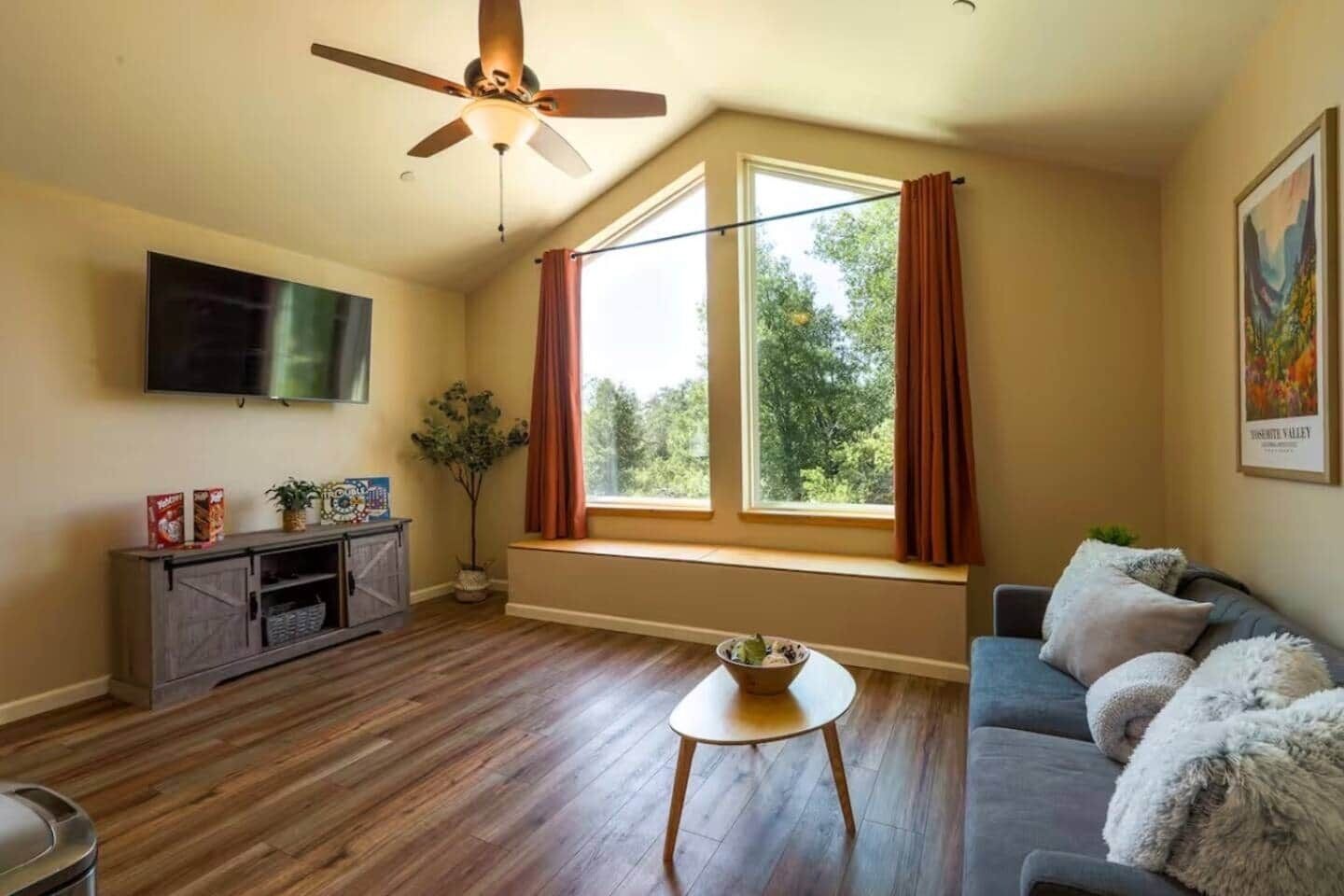 A living room with a ceiling fan, a TV, a window with curtains, a sofa, and a small table with a bowl.
