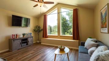 A living room with a ceiling fan, a TV, a window with curtains, a sofa, and a small table with a bowl.