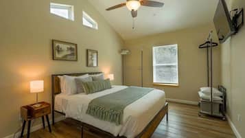 Une chambre à coucher comprenant un lit, des lampes de chevet, un ventilateur de plafond, une fenêtre et un téléviseur fixé au mur.