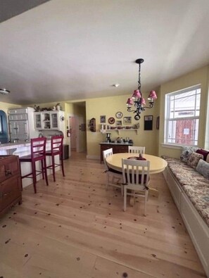 A spacious kitchen with a dining area, wooden flooring, and a large window. - Yosemite Firehouse Inn-Cottage (Mariposa County)