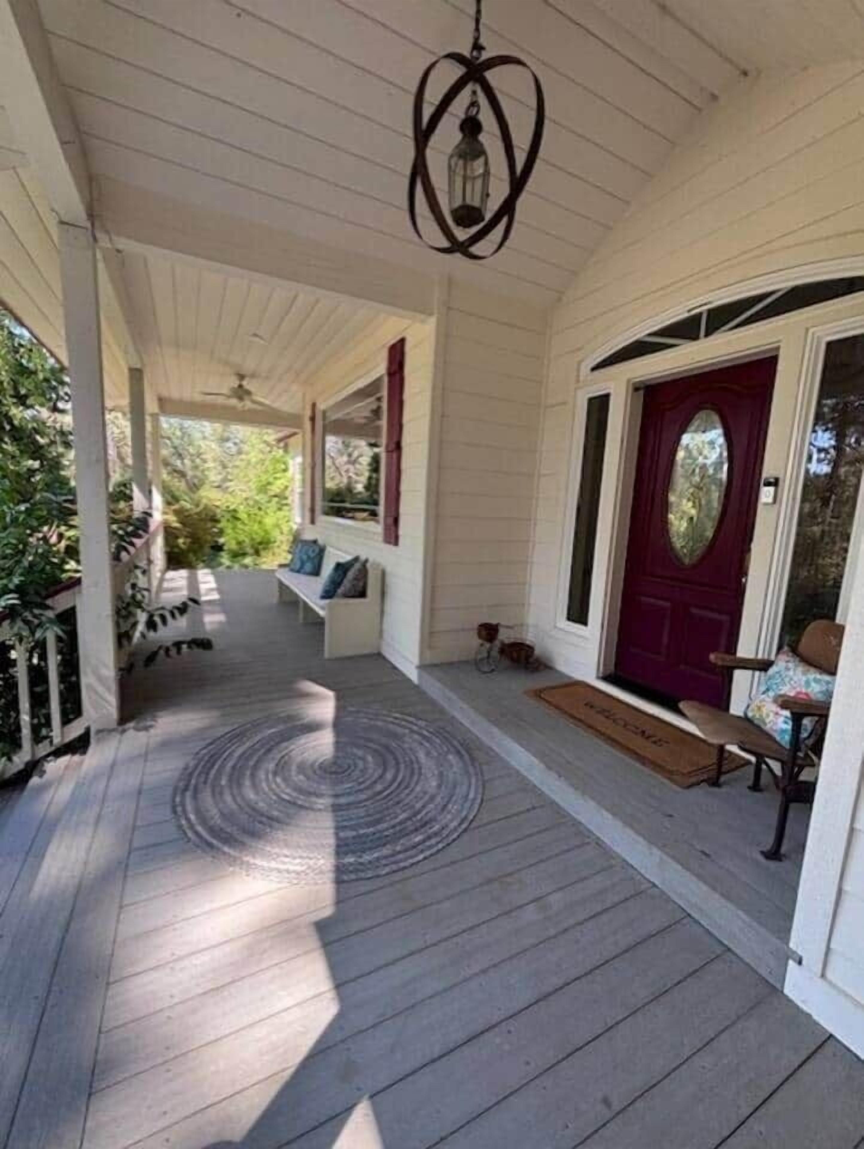 A covered porch with a wooden floor, a red door, and a bench.