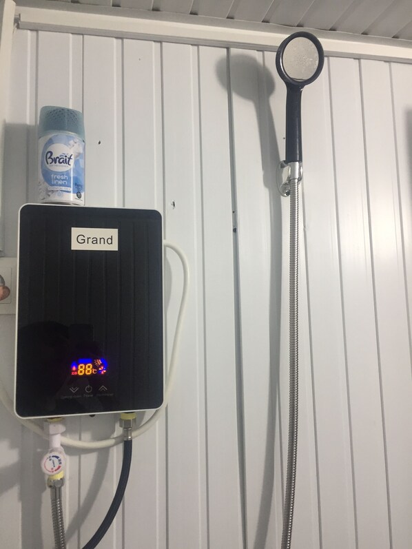 A shower control panel with a digital display, a handheld showerhead, and a bottle of Bralet fresh linen.