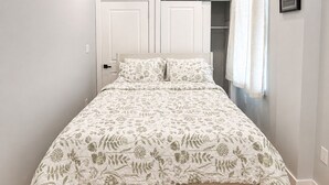 Quarto com cama, guarda-roupa, luminária no teto e janela com cortinas.