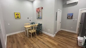 Um quarto com uma mesa de jantar, cadeiras, um refrigerador e um aparelho de ar condicionado.