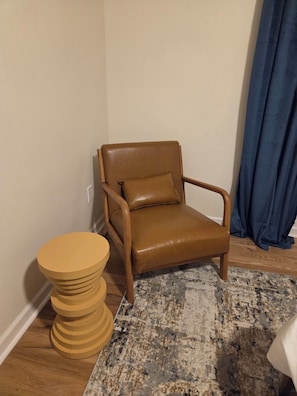 Un fauteuil en cuir marron avec un coussin assorti, une table d’appoint en bois et un tapis à motifs posé sur un plancher en bois.
