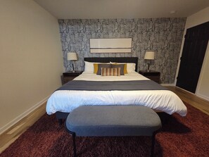A bedroom with a patterned wallpaper, a bed with multiple pillows, a bedside table, and a bench. - 5 Min to Downtown • Hot Tub • Game Room (Atlanta)
