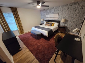 Une chambre à coucher avec un lit, des tables de chevet, un bureau, une chaise, un tapis rouge et un papier peint à motifs.