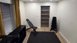 A room with a ceiling fan, a black exercise bench, a stack of dumbbells, a black mat, and a window with blinds. - 5 Min to Downtown • Hot Tub • Game Room (Atlanta)