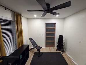 A room with a ceiling fan, a black exercise bench, a stack of dumbbells, a black mat, and a window with blinds. - 5 Min to Downtown • Hot Tub • Game Room (Atlanta)