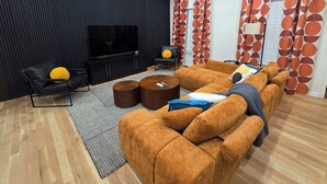 A modern living room with a sectional sofa, a flat-screen TV, a ceiling fan, and patterned curtains. - 5 Min to Downtown • Hot Tub • Game Room (Atlanta)