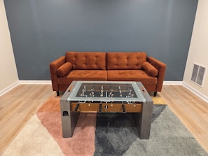Une pièce avec une table de baby-foot, un canapé marron et un tapis à motifs.