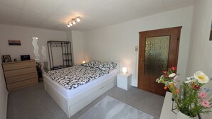 A bedroom with a bed, bedside tables, a dresser, a mirror, a door with a glass panel, and a vase with flowers. - Gemütliche & familienfreundliche Ferienwohnung von HerzZeit- Harz in Wernigerode (Wernigerode)