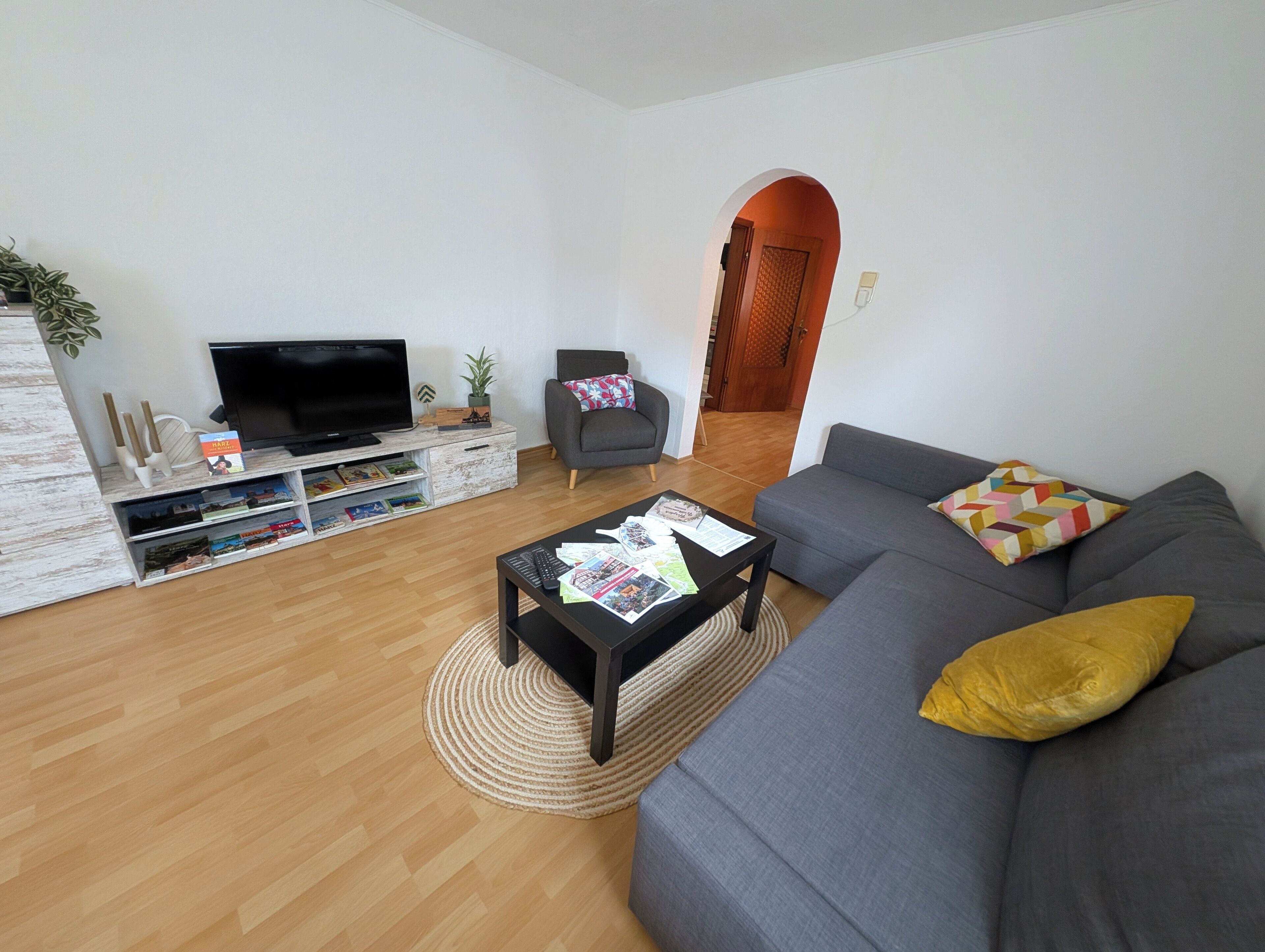 Una sala de estar moderna con televisor de pantalla plana, sofá gris y una mesa de centro con revistas.
