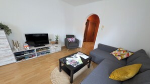 A modern living room with a flat-screen TV, grey sofa, and a coffee table with magazines. - Gemütliche & familienfreundliche Ferienwohnung von HerzZeit- Harz in Wernigerode (Wernigerode)