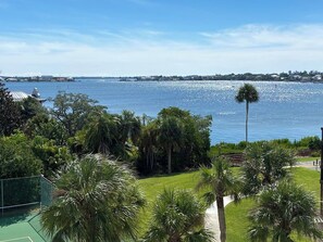 A view of a waterfront property with a tennis court, lush greenery, and a clear blue sky. - Beautiful Condo with Amazing Views, short walk to Siesta Key Beach! Stores close (Sarasota)