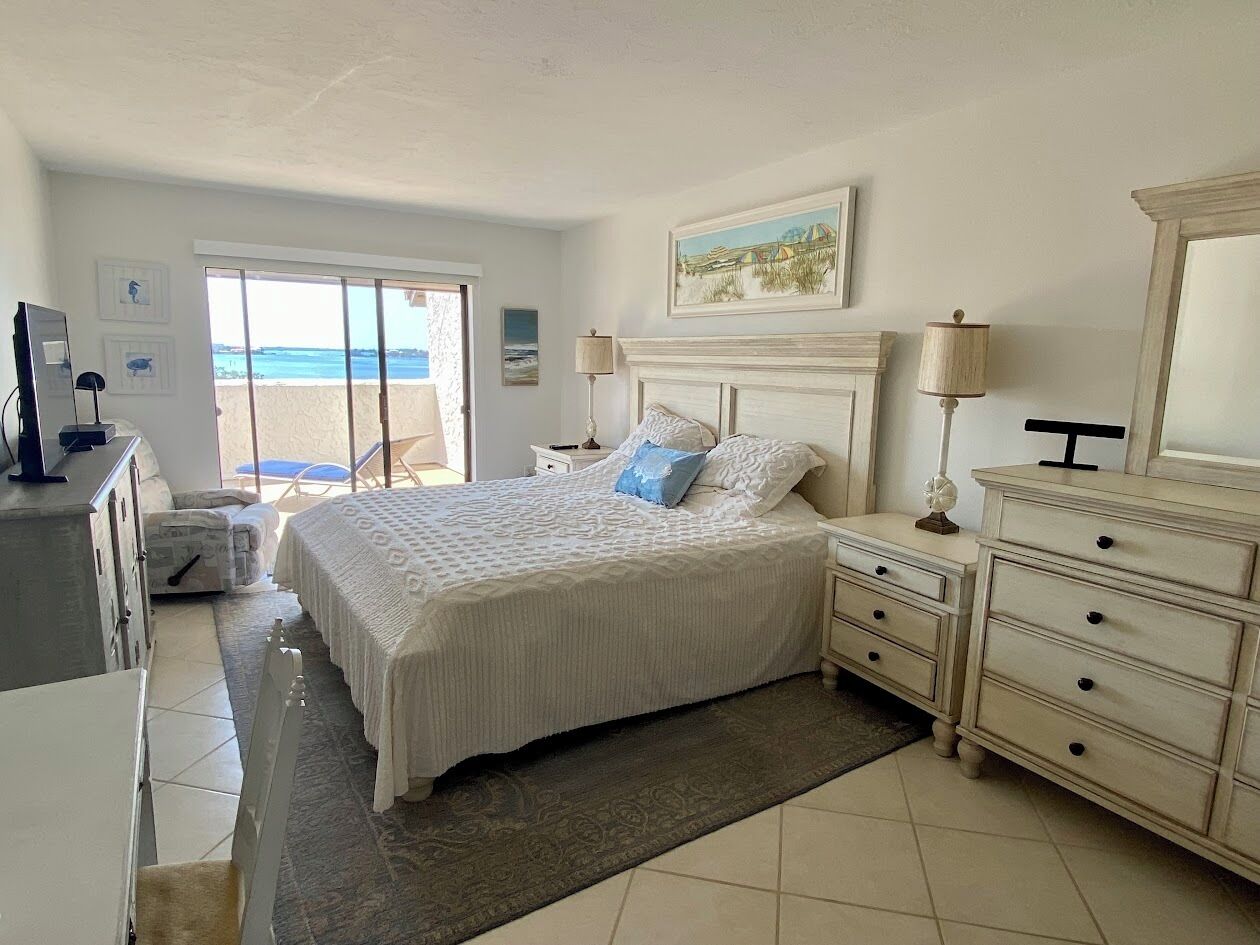 Un dormitorio con cama, mesitas de noche, cómoda y vista a la playa.