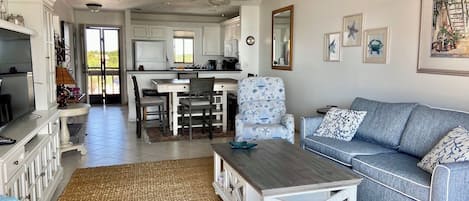 A spacious living area with a sofa, coffee table, and a dining table with chairs. A kitchen is visible in the background.