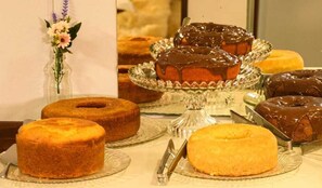 Una mesa con varios pasteles y dulces, incluyendo un pastel cubierto de chocolate sobre un pedestal de vidrio.
