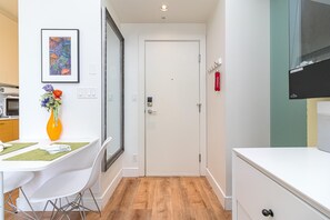 Eine moderne Küche mit weißen Schränken, einem Esstisch mit Stühlen, einer Vase mit Blumen und einem gerahmten Kunstwerk an der Wand.