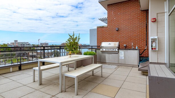 Terraço no telhado com churrasqueira, área de estar e vista para a paisagem urbana.