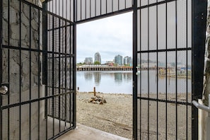 An open metal gate leading to a pebbled waterfront with buildings in the background. - Vibrant Waterfront Living at The Janion (Victoria)