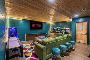 A room with a green sofa, a Netflix sign, and arcade games. - Renovated Playhouse—Slide/Views/Fire Pit/Hot Tub (Pigeon Forge)