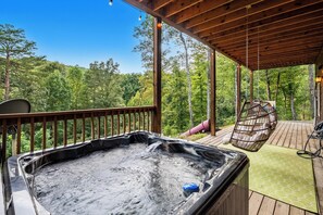 A hot tub on a wooden deck with a hanging chair and a view of a forest. - Renovated Playhouse—Slide/Views/Fire Pit/Hot Tub (Pigeon Forge)