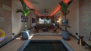 Un intérieur moderne avec un espace salon central, deux grands pots de plantes, un ventilateur de plafond et une vue par la fenêtre.