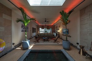 A modern interior with a central seating area, two large potted plants, a ceiling fan, and a view through a window. - Mui Ne Beachside Private Villa (Mũi Né)