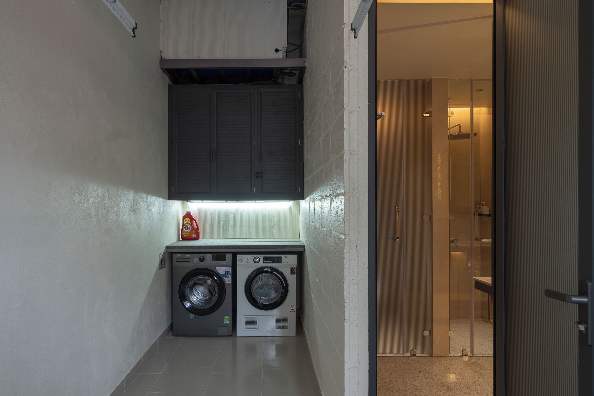 A compact laundry area with two washing machines, a small cabinet, and a glass shower stall.