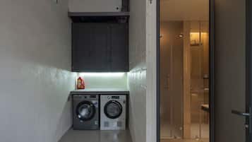A compact laundry area with two washing machines, a small cabinet, and a glass shower stall.