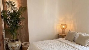 A bedroom with a bed, a nightstand, a lamp, a potted plant, and a woven basket.