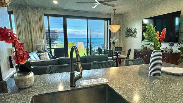 A modern kitchen with a granite countertop, a stainless steel sink, and a dining area with a view of the ocean. - Oceanfront, swim with turtles, enjoy sunset views, all from your backyard. #B18 (Lahaina)