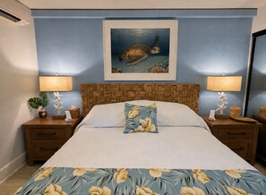 Ein Schlafzimmer mit einem Bett, Nachttischen, einem Bild einer Meeresschildkröte und einer blumigen Tagesdecke.